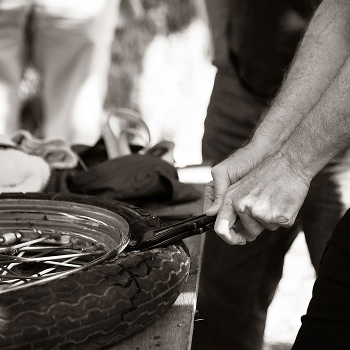 Black and white image of two hands fixing a motorcycle tire. Photo credit: Chris Smith, Chris and Cami Photography.
