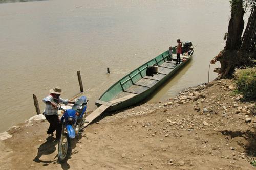 Boatman loading smaller 100cc motorcycle into boat.