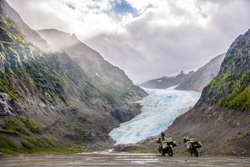 Photo by Bettina Hoebenreich (Germany) of herself in British Columbia, Canada, dwarfed by the massive, eternally-enduring ice of Bear Glacier. RTW tour in 2016 on our 1989 and 1993 Honda Transalps.