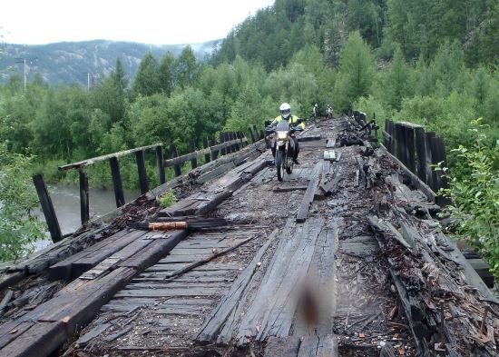 Lorraine Spence, crossing a rickety wooden bridge by motorcycle.