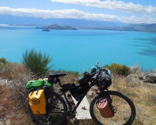 Nevil Stow, Bikepacking next to an azure lake.