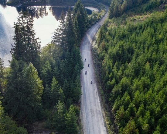 Suzanne Jolly, A Wilder Way aerial of riders on forested lake-side dirt road.