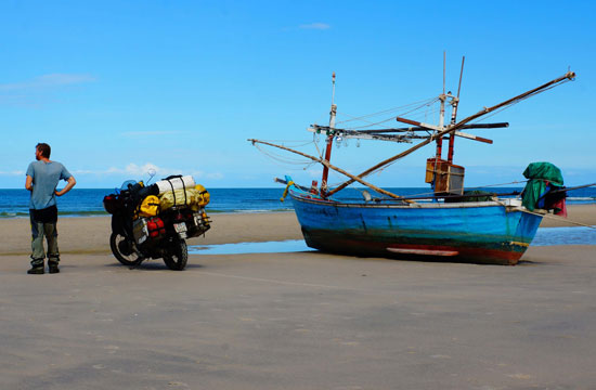 Christian with bike and boat on beach.