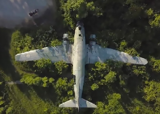 Aerial of a motorcycle and an airplane wreck among trees.