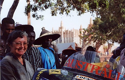 Locals gathering around the motorcycle with mud mosque in the background